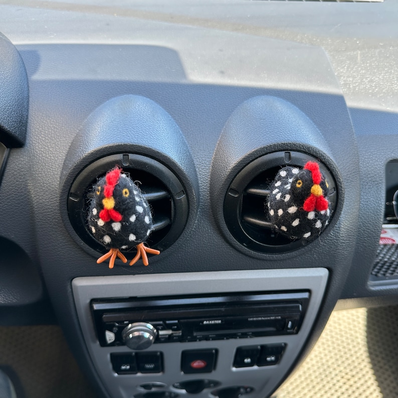 Puede incluir: Dos ambientadores con forma de pollo a lunares blancos y negros, con crestas rojas y picos amarillos, est&aacute;n insertados en las rejillas de ventilaci&oacute;n del salpicadero de un coche. Los pollos tienen patas naranjas y est&aacute;n hechos de un material suave.