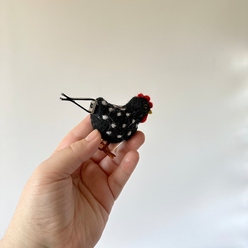 Puede incluir: Pinza para el pelo con forma de gallina negra con lunares blancos, cresta roja y pico amarillo. La pinza es de fieltro y tiene patas marrones. Un accesorio para el cabello &uacute;nico.
