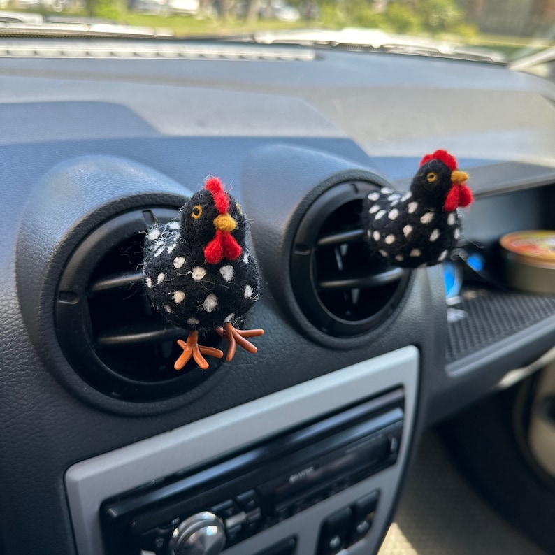 Puede incluir: Dos ambientadores con forma de pollo negro con lunares blancos, con crestas rojas y picos amarillos, est&aacute;n sujetos a las rejillas de ventilaci&oacute;n del salpicadero de un coche. Los pollos tienen patas naranjas y est&aacute;n hechos de un material suave.