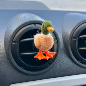 K&ouml;nnte beinhalten: Ein Filz-Enten-Lufterfrischer f&uuml;r das Auto mit gr&uuml;nem Kopf, braunem K&ouml;rper und orangefarbenen F&uuml;&szlig;en. Die Ente h&auml;ngt an einer L&uuml;ftung im Auto.