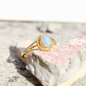 Könnte beinhalten: Ein goldener Ring mit einem weißen Opal-Edelstein, der in einer Perlenfassung sitzt. Der Ring hat ein zartes, durchbrochenes Design.