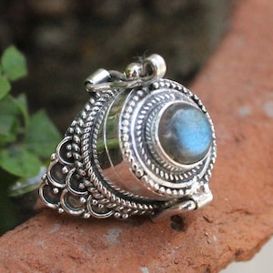 May include: A silver ring with a hinged compartment and a blue labradorite gemstone. The ring is intricately detailed with a rope-like design and floral accents.
