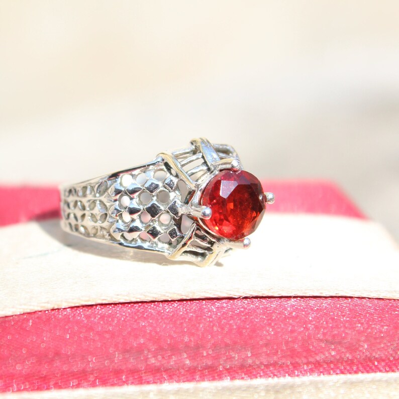 May include: A silver ring with a red gemstone set in a delicate, intricate design.