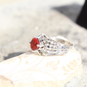 May include: A silver ring with a red gemstone set in a filigree design.