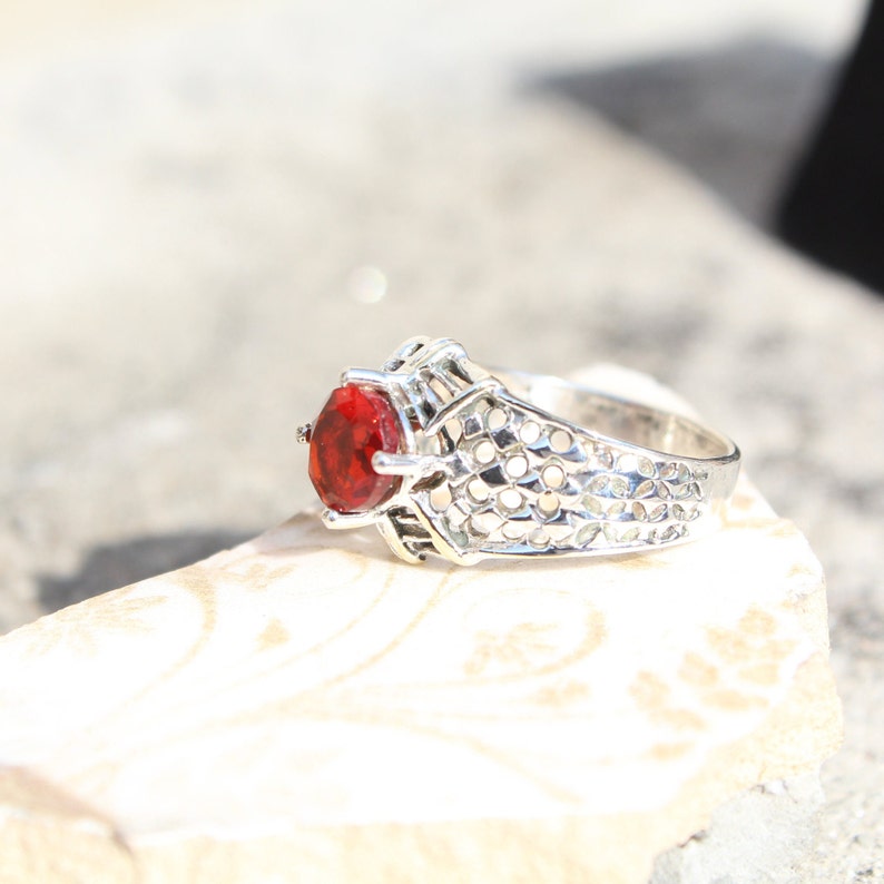 May include: A silver ring with a red gemstone set in a filigree design.