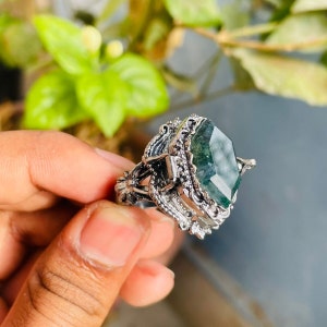 May include: A silver ring with a large, green, faceted gemstone set in a detailed, ornate design.