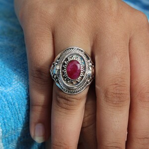 May include: A silver ring with an ornate design and a large, oval-shaped ruby gemstone.