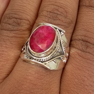 May include: A silver ring with a large, oval-shaped, red gemstone set in a decorative silver bezel. The ring has a wide band with intricate details.