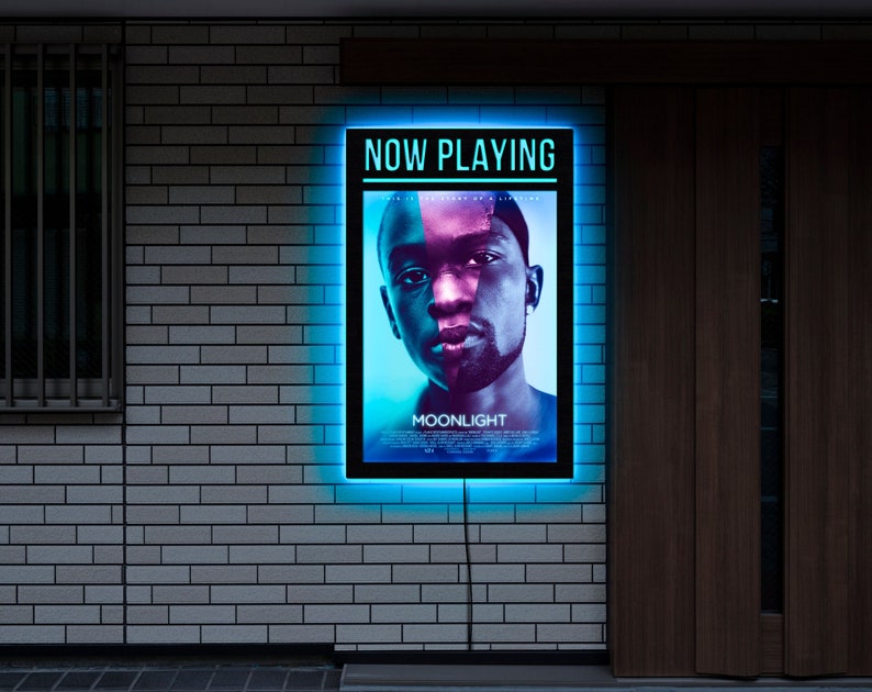 May include: A blue neon sign with the words "NOW PLAYING" and the movie title "MOONLIGHT" in white text. A black and white image of a man's face is in the center of the sign.