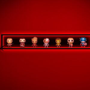 May include: A black rectangular shelf with red LED lighting, displaying seven character figurines. The figurines are of various colors and designs, including a guitar player, a warrior, and Captain America. The shelf is mounted on a red wall.