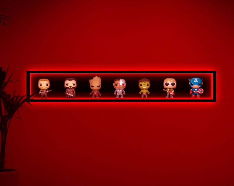 May include: A black rectangular shelf with red LED lighting, displaying seven character figurines. The figurines are of various colors and designs, including a guitar player, a warrior, and Captain America. The shelf is mounted on a red wall.