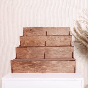Peut inclure: Pr&eacute;sentoir en bois &agrave; quatre niveaux. Le pr&eacute;sentoir est en bois teint&eacute;, avec un design en gradins. Le grain du bois est visible. Con&ccedil;u pour exposer des objets, chaque niveau offrant une surface.