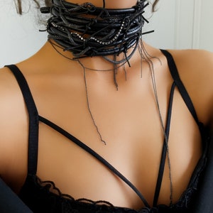 Leather choker necklace is created by the combination of 5 rows of leather, with crystals accompanying these rows. A snake chain weaves between these leather rows, completing this leather choker with a chain that extends to the chest