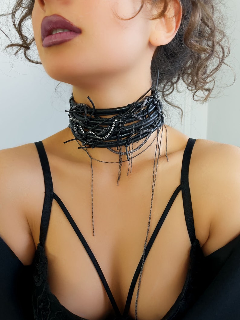 Leather choker necklace is created by the combination of 5 rows of leather, with crystals accompanying these rows. A snake chain weaves between these leather rows, completing this leather choker with a chain that extends to the chest