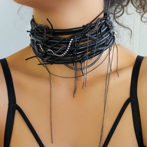 Leather choker necklace is created by the combination of 5 rows of leather, with crystals accompanying these rows. A snake chain weaves between these leather rows, completing this leather choker with a chain that extends to the chest