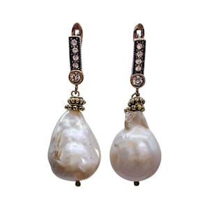 May include: A pair of silver earrings with a baroque pearl drop and a crystal-encrusted bar. The pearls are white and the crystals are clear.