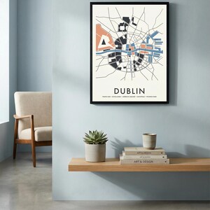 Könnte beinhalten: Ein gerahmter Stadtplan von Dublin, Irland, mit minimalistischem Design. Die Karte zeigt eine schwarze Umrandung mit Bereichen, die in Schwarz, Blau und Pfirsich gefüllt sind. Das Wort "DUBLIN" ist darunter in fetter Schrift gedruckt.