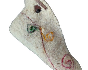 May include: A white felt slipper with a brown leather tag that says "Stella" and colorful embroidery. The embroidery includes a green and yellow design, a red swirl, and a yellow flower.