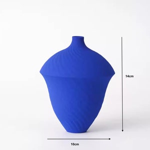 Può includere: Un vaso decorativo blu cobalto con una forma organica unica. Il vaso è alto circa 14 cm e largo 10 cm. La superficie presenta un motivo a spirale strutturato. Il vaso ha un collo stretto e un corpo ampio e svasato.