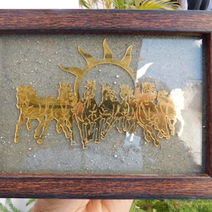 Op de afbeelding: Een ingelijst kunstwerk met een gouden zon en paarden. De paarden rennen op een getextureerde, lichtgrijze achtergrond. De lijst is donkerbruin, geschikt voor interieurdecoratie.