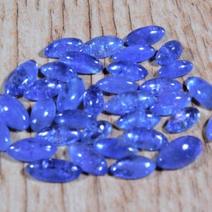 May include: A collection of oval-shaped blue gemstones, likely blue topaz or aquamarine, arranged on a wooden surface.