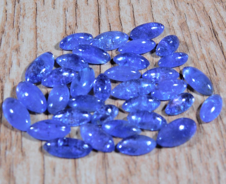 May include: A collection of oval-shaped blue gemstones, likely blue topaz or aquamarine, arranged on a wooden surface.