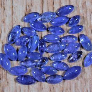 May include: A collection of oval-shaped, blue gemstones, likely blue topaz or aquamarine, arranged in a circular pattern on a wooden surface.