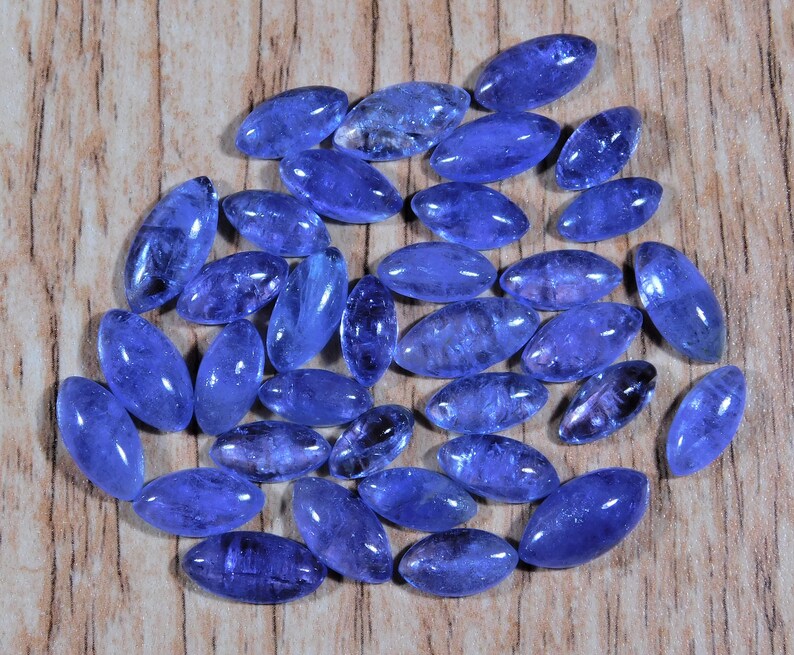 May include: A collection of oval-shaped, blue gemstones, likely blue topaz or aquamarine, arranged in a circular pattern on a wooden surface.