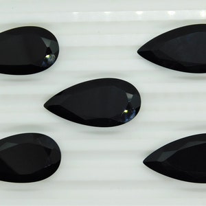 May include: Five black pear-shaped gemstones on a white surface. The gemstones are faceted and have a glossy finish.