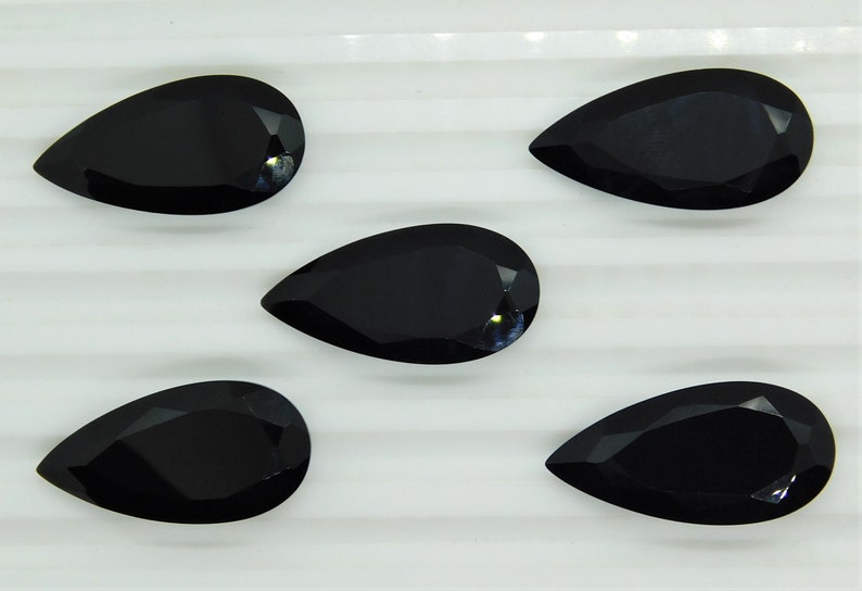 May include: Five black pear-shaped gemstones on a white surface. The gemstones are faceted and have a glossy finish.