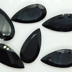 May include: Six black pear-shaped gemstones on a white background. The gemstones are faceted and have a glossy finish.