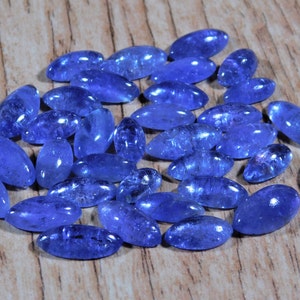 May include: A collection of 25 oval-shaped, blue gemstone cabochons. The stones are smooth and polished, with a slight shimmer.