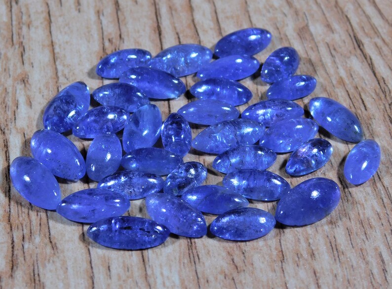 May include: A collection of 25 oval-shaped, blue gemstone cabochons. The stones are smooth and polished, with a slight shimmer.