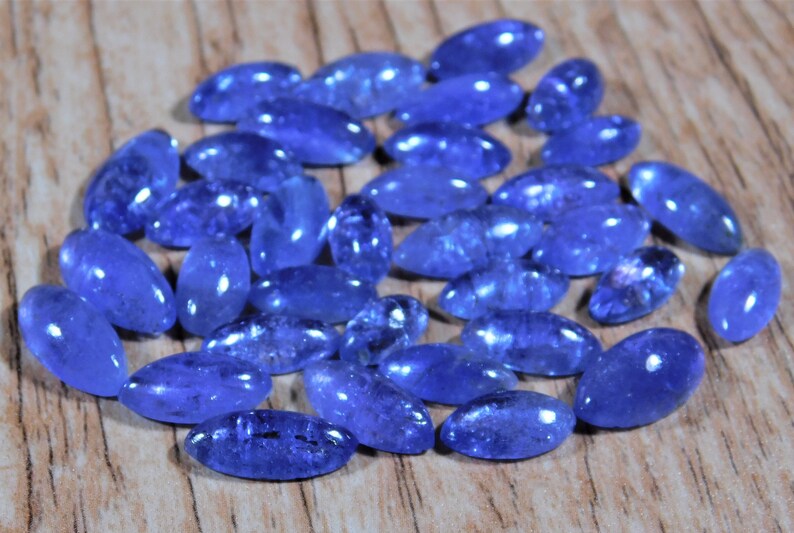 May include: A collection of oval-shaped, blue gemstones. The gemstones are smooth and polished, with a slight shimmer.