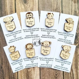 May include: Eight wooden pocket hug cards with different animal designs. Each card has a pocket with a small wooden animal inside. The cards have the text "Pocket Hug" and a message about showing someone you care.