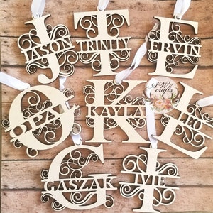 May include: A collection of eight wooden ornaments, each featuring a different letter of the alphabet with a decorative flourish. The letters are painted white and have names written across the center of each letter. The names are: Jason, Trinity, Ervin, Opa, Kayla, Leo, Gaszak, and Ivie.