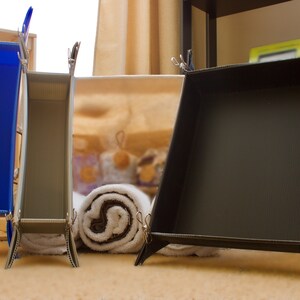May include: Three black plastic trays with clips, two are tall and narrow, one is wide and shallow. The trays are standing on a light brown surface.