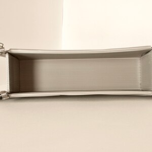 May include: A white, rectangular, foldable storage box with silver clips on each corner. The box is empty and open.