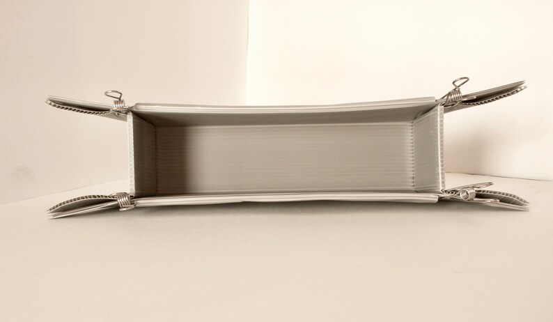 May include: A white, rectangular, foldable storage box with silver clips on each corner. The box is empty and open.