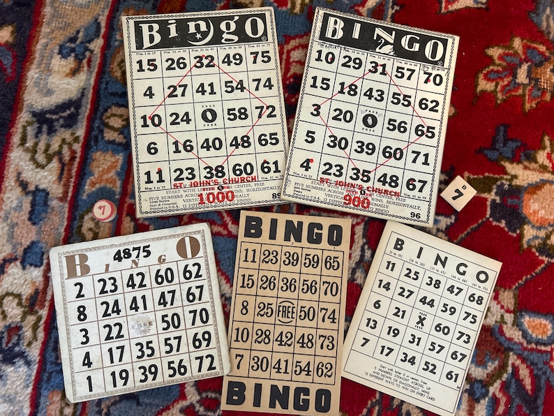 Pu&ograve; includere: Sei cartelle del bingo con numeri da 1 a 75. Le cartelle sono bianche con numeri neri e un titolo nero "Bingo". Le cartelle sono su una superficie con un motivo rosso e dorato.