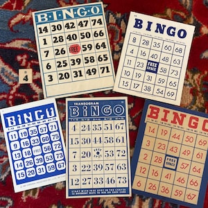 Pu&ograve; includere: Quattro carte da bingo blu e bianche con numeri e la parola "BINGO" in rosso. Le carte sono su una superficie con motivo rosso e blu.