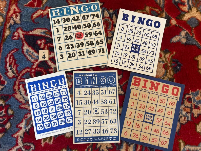 Pu&ograve; includere: Quattro carte da bingo blu e bianche con numeri e la parola "BINGO" in rosso. Le carte sono su una superficie con motivo rosso e blu.