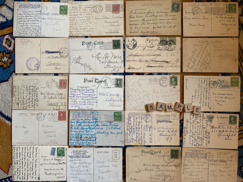 May include: A collection of vintage postcards with handwritten messages. The postcards are in various colors and feature different designs, including a landscape scene, a building, and a floral pattern. The postcards are all in good condition and have been well-preserved.