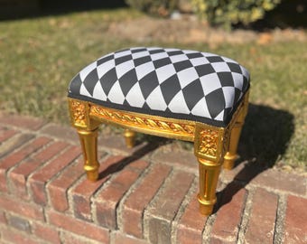 May include: A black and white checkered fabric footstool with gold painted legs and ornate details.