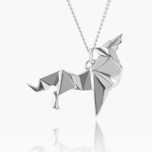 Puede incluir: Colgante de lobo origami plateado sobre una fina cadena. El colgante representa un lobo aullando en un estilo geométrico. La cadena es de tipo cuentas. Una joya llamativa.