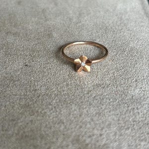 Puede incluir: Un anillo de oro rosa con un diseño de estrella de cinco puntas que presenta un pequeño diamante en el centro.