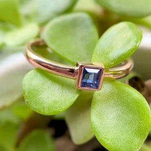 Puede incluir: Un anillo de oro con una piedra preciosa azul cuadrada engastada en garras.
