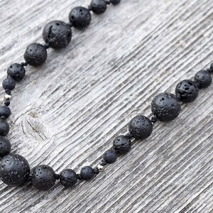 Könnte beinhalten: Eine schwarze Lava-Perlenkette mit silbernen Akzenten. Die Kette besteht aus natürlichen Lava-Perlen und ist auf einer schwarzen Schnur aufgefädelt.