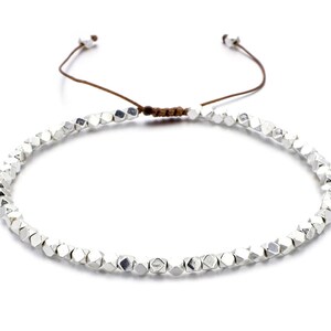May include: A silver beaded bracelet with a brown cord closure. The beads are faceted and have a metallic finish.
