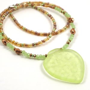 May include: A green glass heart pendant necklace with a brown and green beaded chain. The heart pendant has a textured surface.